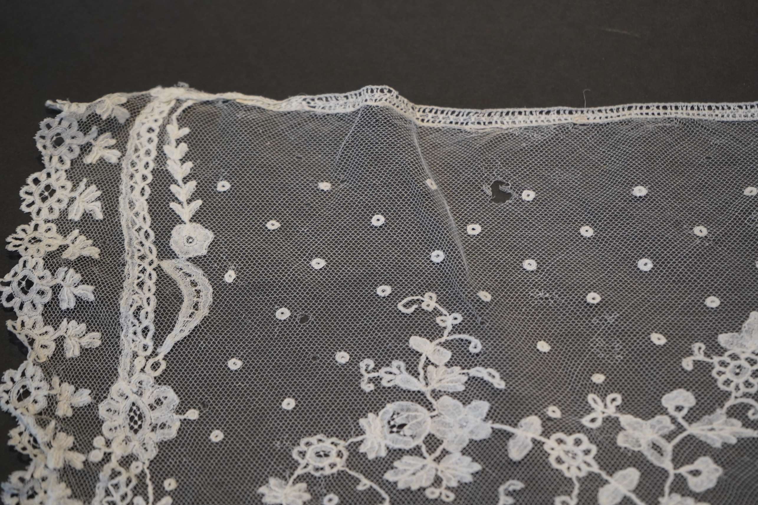 A deep elaborately designed flounce of mid 19th century Brussels bobbin appliquéd lace on net, with finished lace ends, worked with an intricate floral border below large floral cartouches framed in similar motifs and al